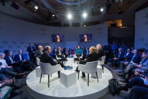 Evento presencial com televisões atrás dos palestrantes mostrando transmissão ao vivo dos palestrantes